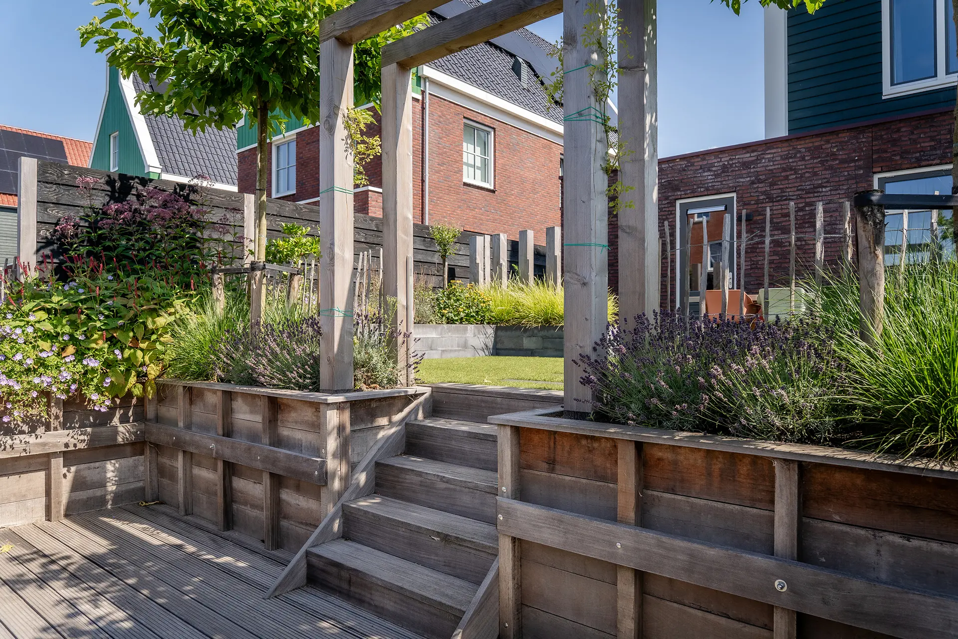 In een moderne nieuwbouwwijk hebben we deze tuin ontworpen en aangelegd rondom een veranda, aangelegd door Uw Verandaspecialist. Het strakke ontwerp is gecombineerd met warme materialen zoals houten palen en een zweefbank op de plantenborder. Zo ontstond een tuin die strak oogt maar tegelijk gezellig en uitnodigend is. De staptegels in het gazon zorgen voor rust en structuur, terwijl de weelderige border aan het water voor levendigheid en kleur zorgt. Een tuin waarin ontwerp, materiaalgebruik en beplanting mooi in balans zijn en samen zorgen voor een sfeervol geheel.