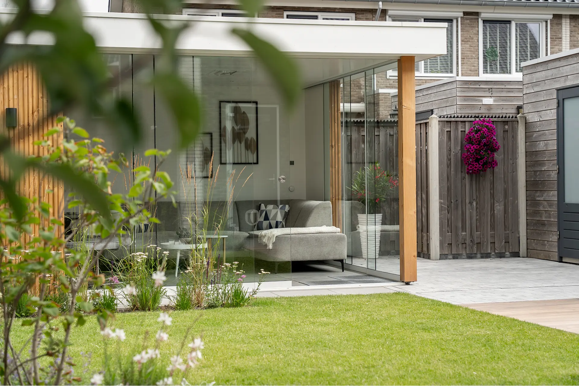 In Julianadorp hebben we gewerkt aan een moderne tuin met een rustige, luxe uitstraling. De tuinkamer is een echte verrijking van de woning. De stijl ervan hebben we doorgetrokken in het ontwerp, zodat huis en tuin één geheel vormen.
De combinatie van strakke lijnen, witte plantenbakken en natuurlijke materialen zoals hout en lichte tegels geeft de tuin het gevoel van een poolhouse. Een plek waar binnen en buiten moeiteloos in elkaar overlopen. De beplanting zorgt voor kleur en levendigheid, waardoor het geheel in balans blijft. Een tuin met uitstraling en comfort, waar alles klopt tot in de details.