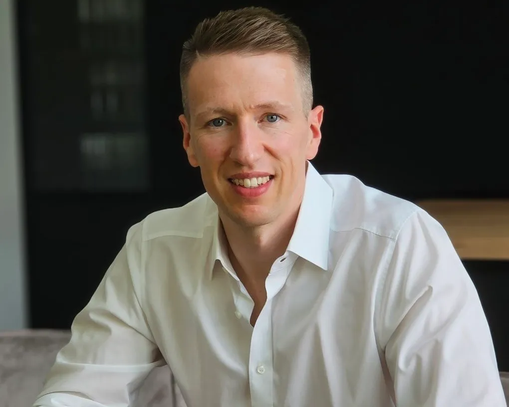 Jannis Gerlinger lächelt freundlich in die Kamera und trägt ein weißes Hemd in einem modernen Büro.