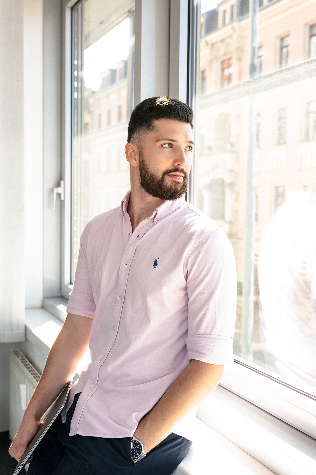 Lukas Janik lehnt mit einem Laptop in der Hand am Fenster eines Büros und blickt nach draußen.