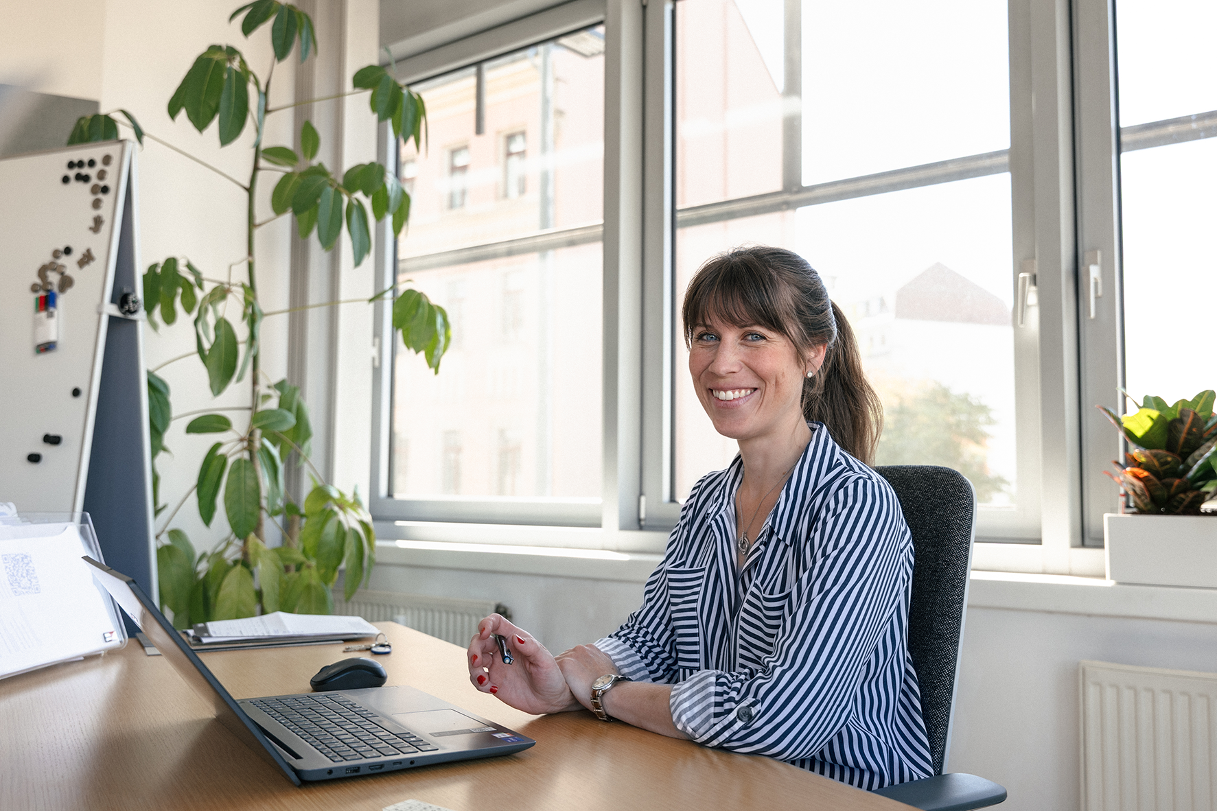 Julia Müller sitzt an einem Schreibtisch im Büro und lächelt in die Kamera, vor ihr ein Laptop.