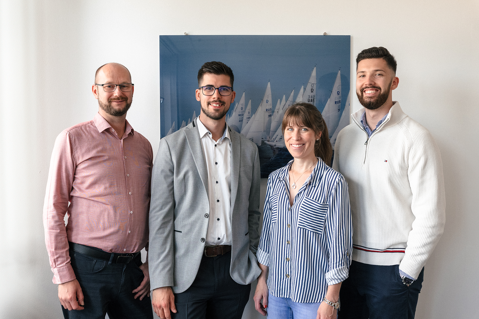 Vier Teammitglieder der Provenia Lösungen GmbH stehen nebeneinander vor einem Bild mit Segelbooten und lächeln.