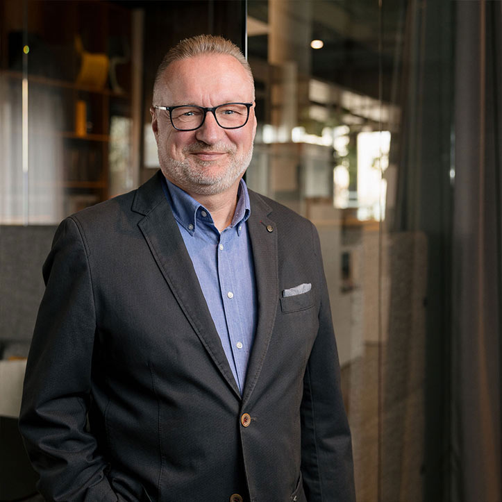 Mann mit Brille und Anzug steht in professionellem Umfeld.