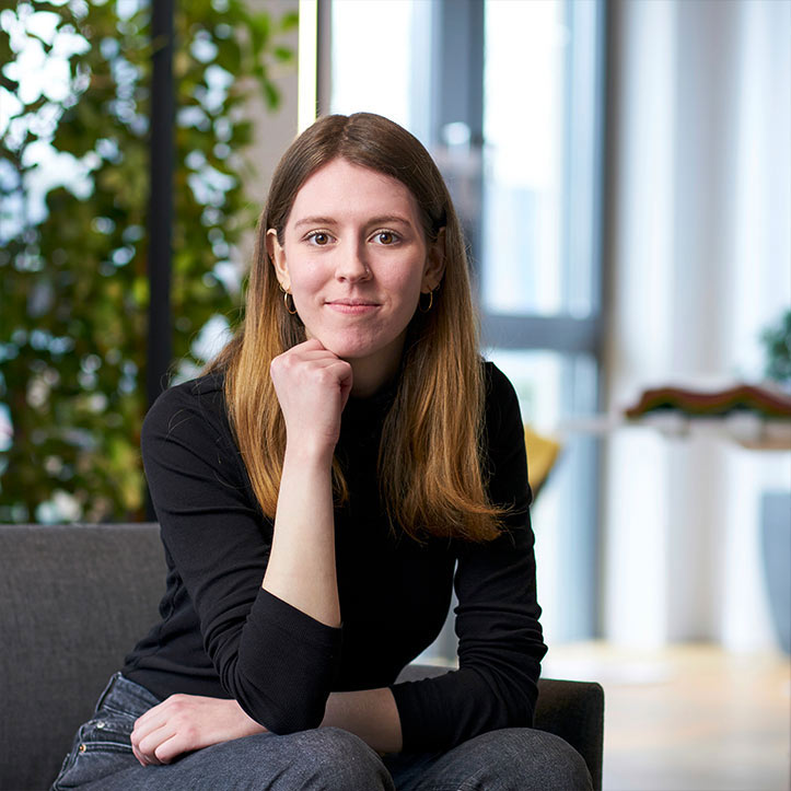 Frau mit nachdenklicher Pose sitzt in hellem Bürobereich.