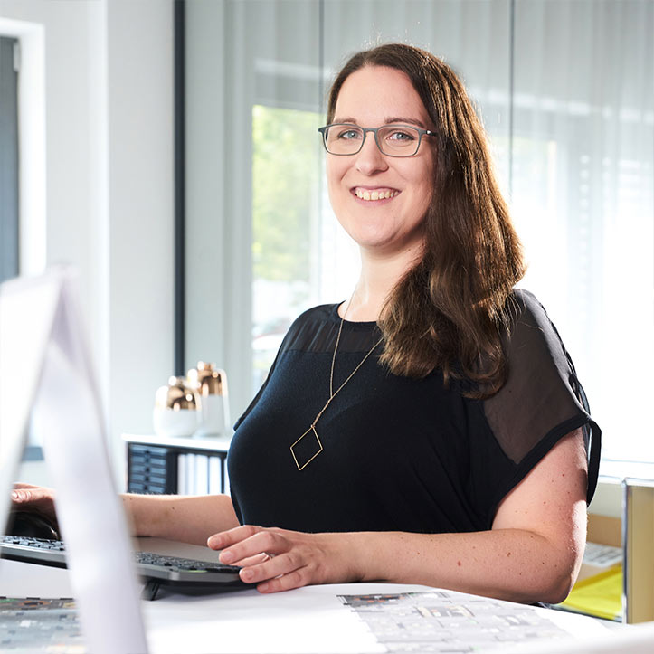 Frau arbeitet lächelnd am Computer in heller Büroatmosphäre.