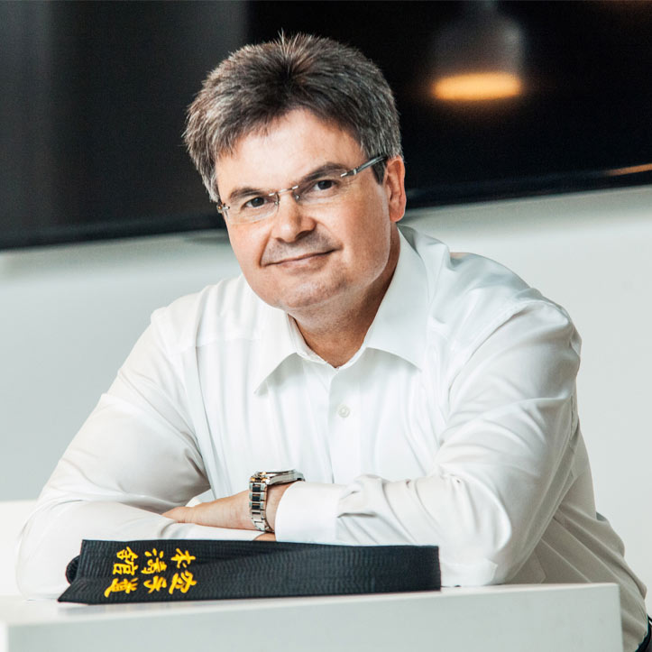 Mann im weißen Hemd lächelt an einem Schreibtisch.