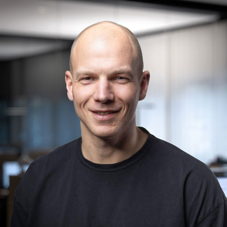 Mann mit Glatze trägt schwarzes Shirt und blickt freundlich in die Kamera.