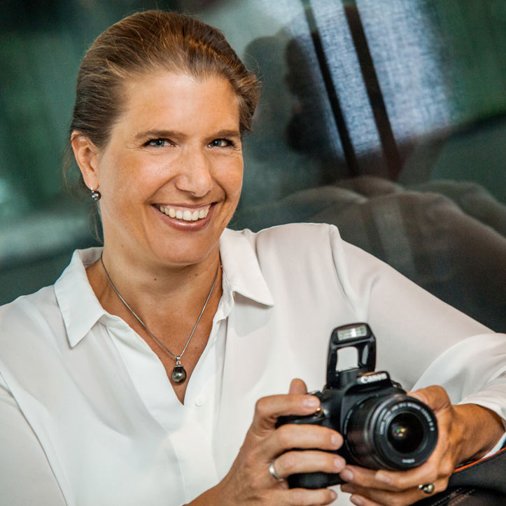 Frau mit Kamera lächelt freundlich in modernem Umfeld.