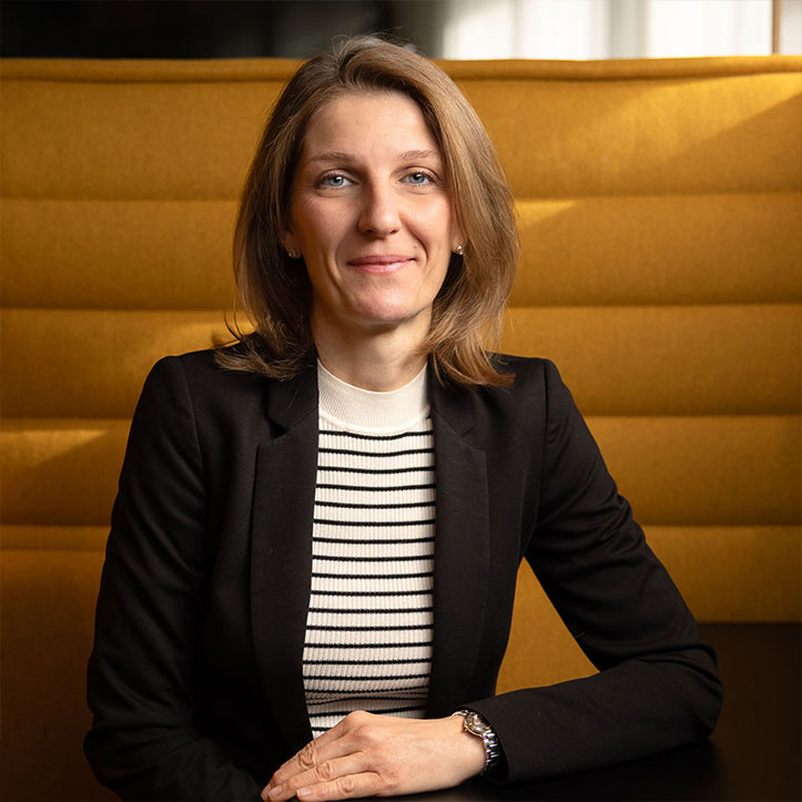 Frau mit Blazer und Streifenshirt sitzt in gelber Sitznische.