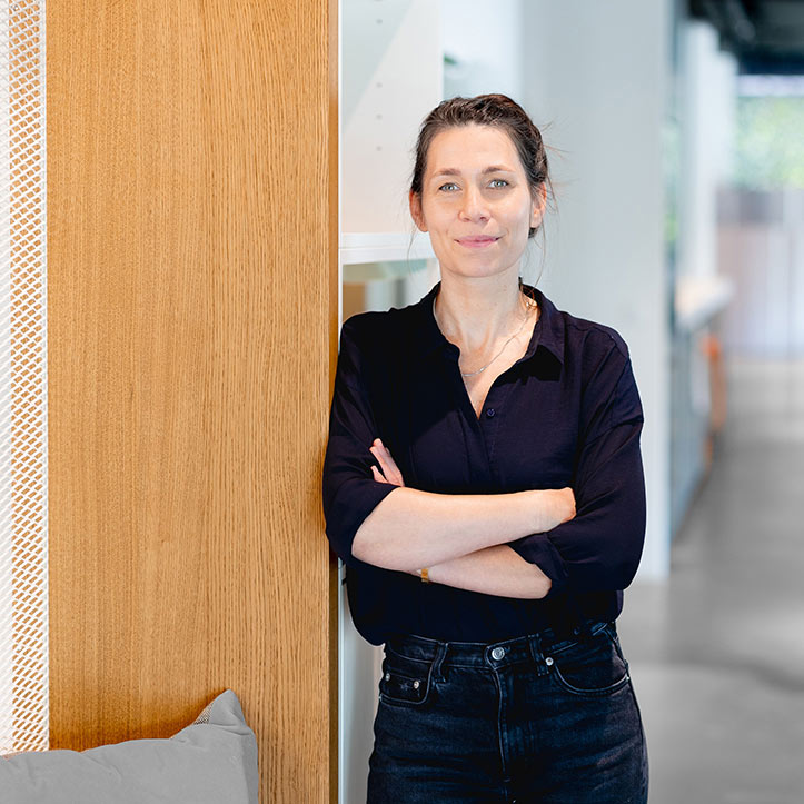 Frau mit verschränkten Armen lehnt an einer Holzsäule im Büro.