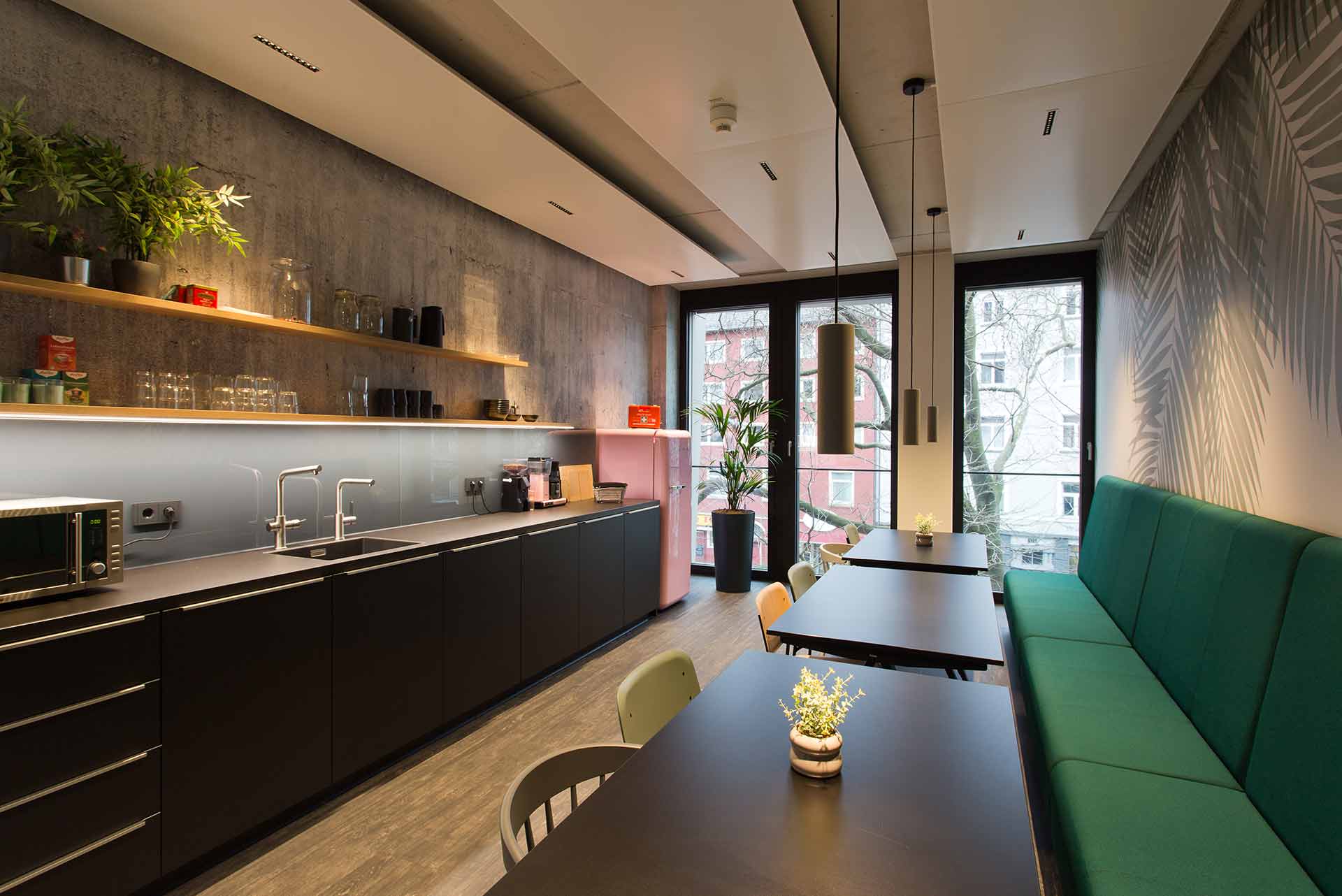 Moderne Büroküche mit dunklen Schränken, grüner Polsterbank und warmem Licht.
