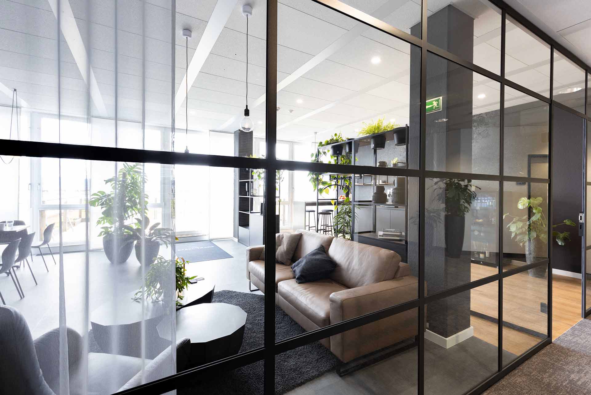 Helle Lounge mit Glaswänden, gemütlichen Sitzmöbeln und natürlichem Lichteinfall.