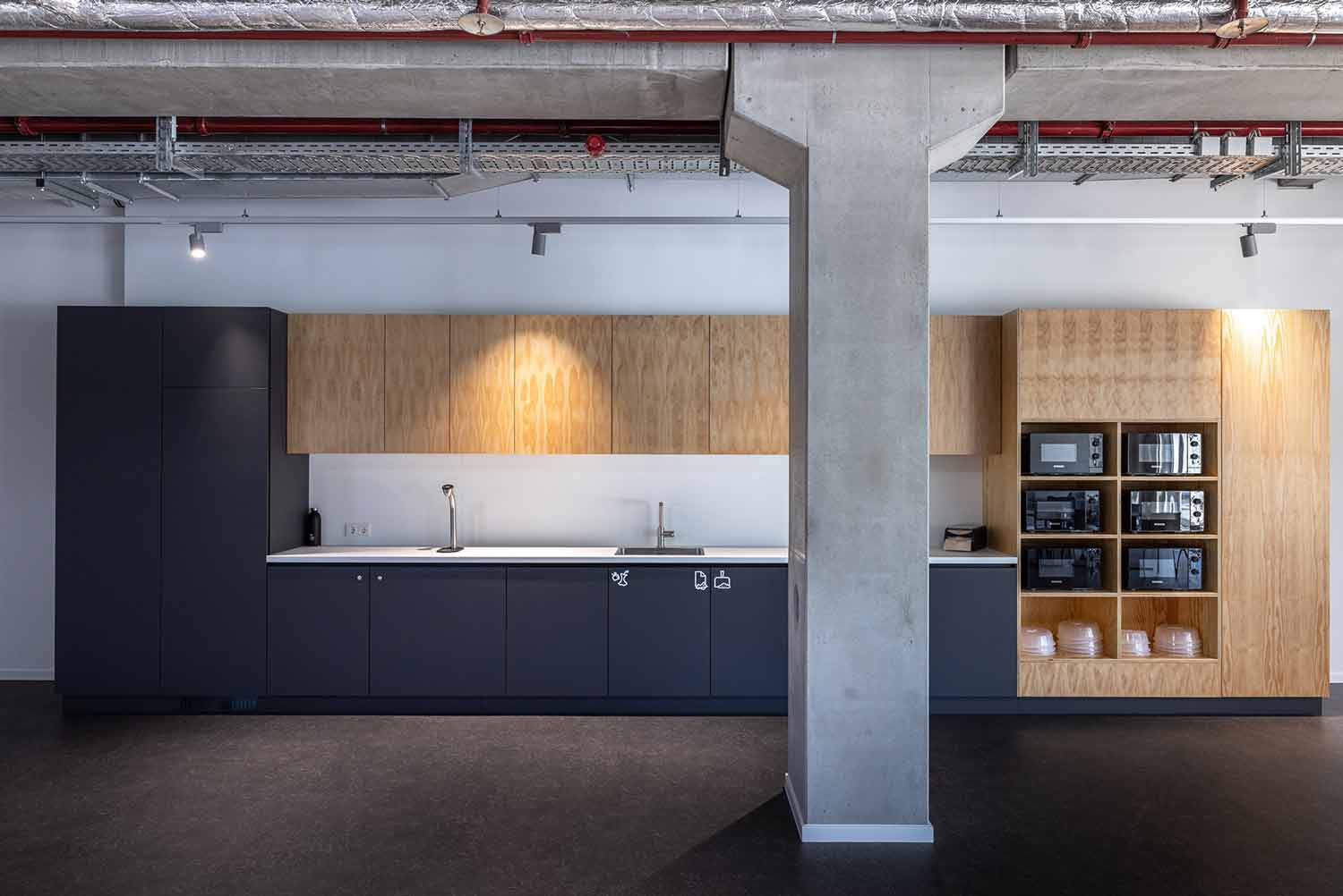 Moderne Büroküche mit Betonpfeiler, Holzfronten und minimalistischer Gestaltung.