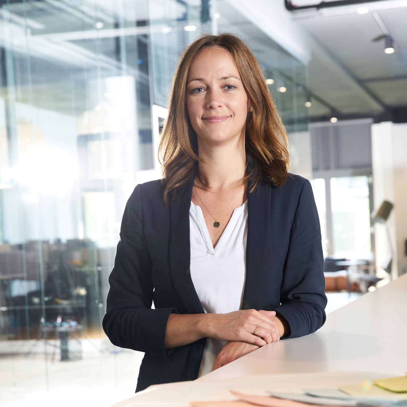 Geschäftsfrau mit offenem Haar lächelt selbstbewusst in einem modernen Büro.

