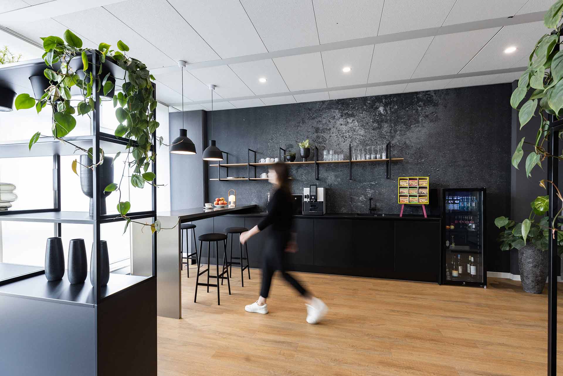 Moderne Büro-Kaffeebar mit dunkler Einrichtung und Pflanzenakzenten.