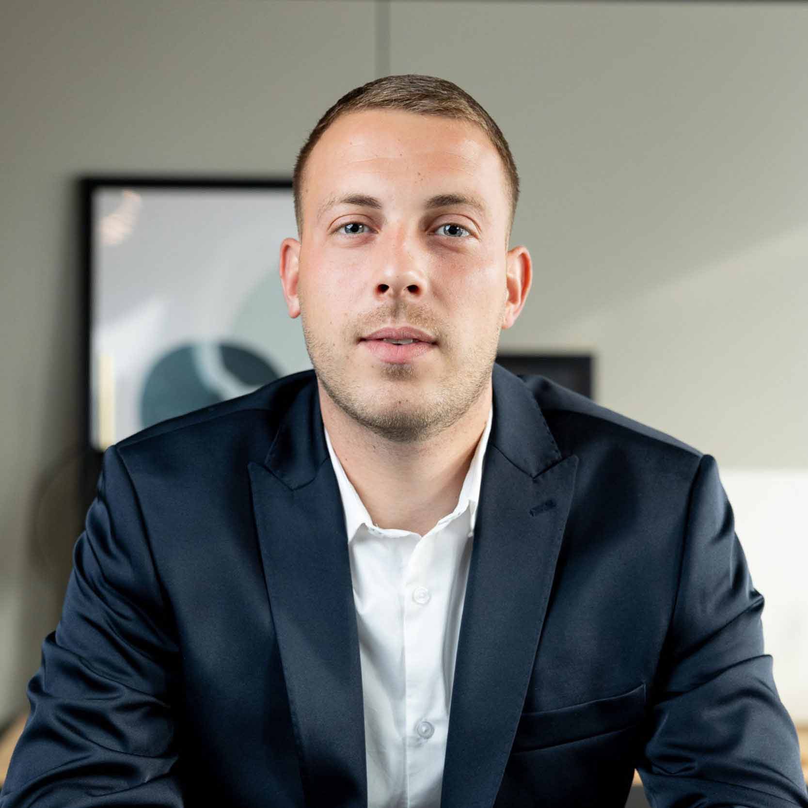 Geschäftsmann im Anzug blickt selbstbewusst in die Kamera.