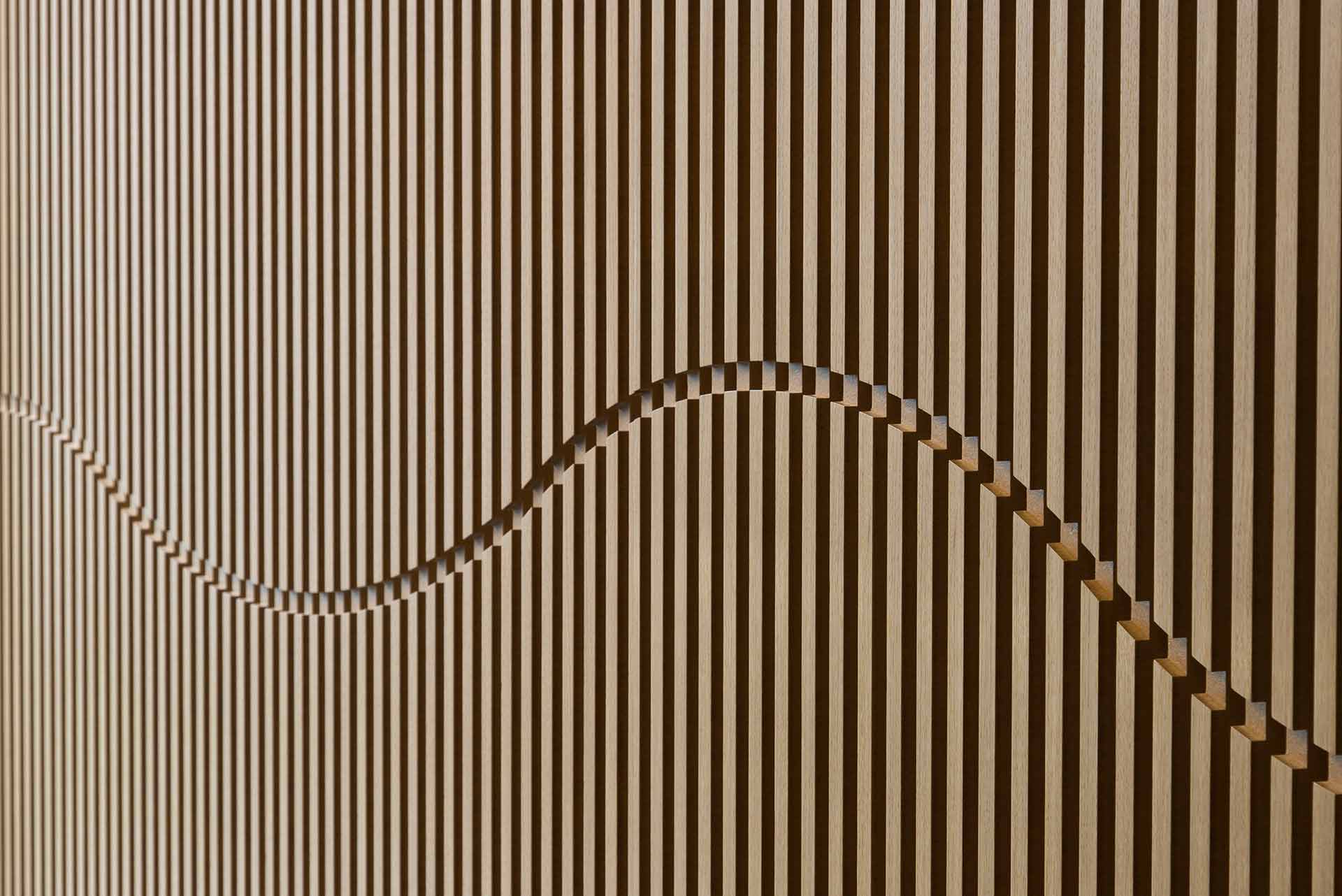 Holzwand mit vertikalen Lamellen und einem wellenförmig geschnitzten Muster.