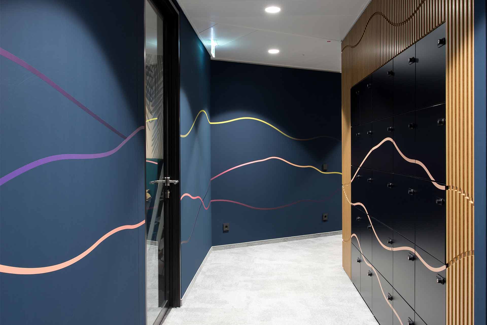 Moderner Flur mit dunkelblauen Wänden, bunten wellenförmigen Linien und schwarzen Spinden, die von vertikalen Holzlamellen eingerahmt sind.