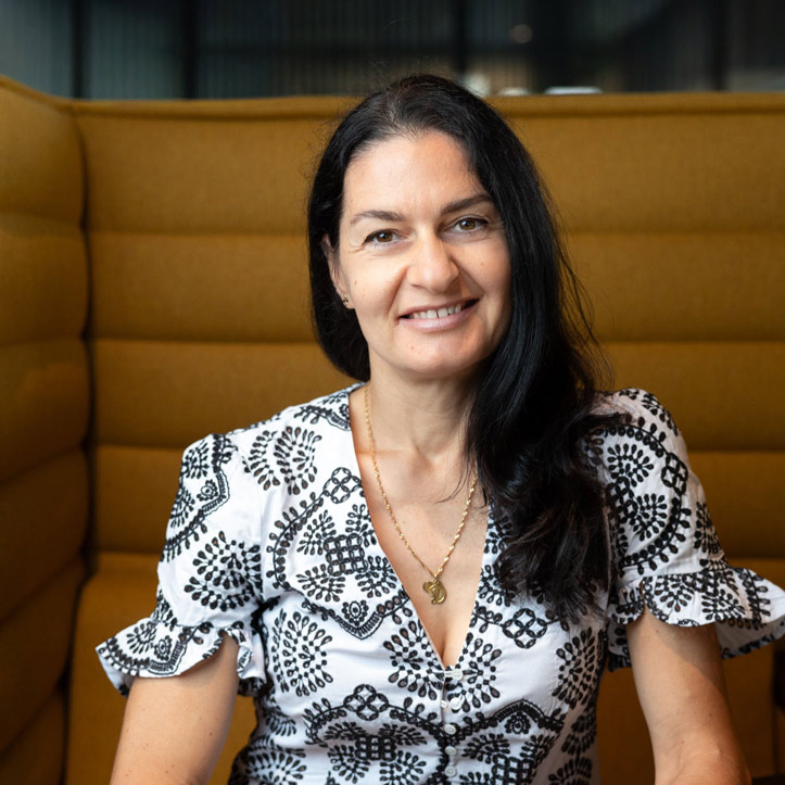 Frau in gemustertem Kleid sitzt lächelnd in einer gemütlichen Büro-Lounge.

