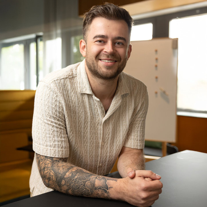 Lächelnder Mann in hellem Hemd sitzt entspannt in einem modernen Büro.