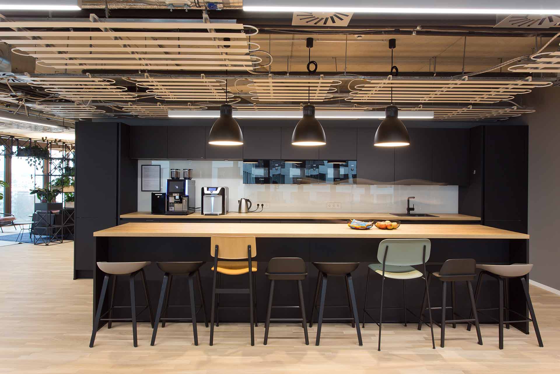 Moderne Büroküche mit Holzdetails und langen Tischen in warmem Licht.