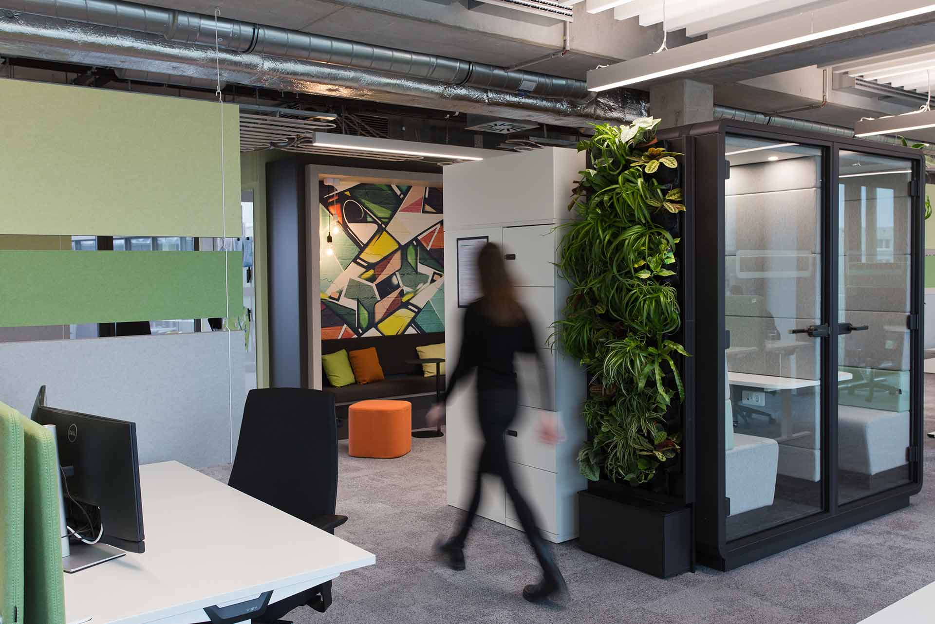 Moderne Bürofläche mit Glaswänden, begrüntem Wandmodul und dynamischer Arbeitsatmosphäre.