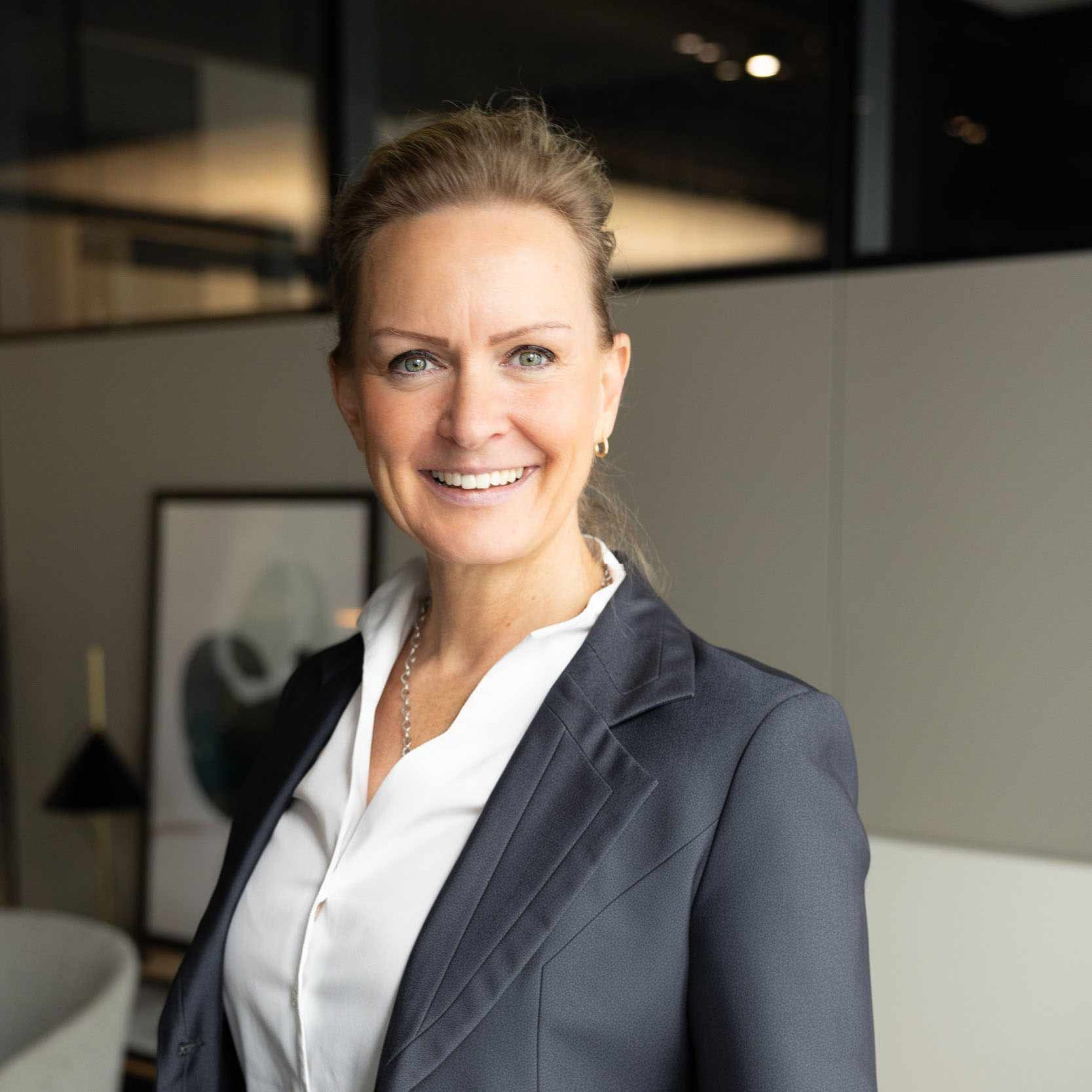 Geschäftsfrau in elegantem Anzug lächelt selbstbewusst in einem Büro.