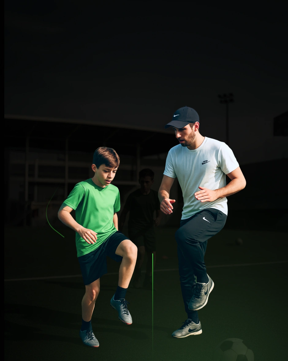 Un allenatore con cappellino nero e t-shirt bianca insegna a un ragazzo con maglietta verde esercizi di coordinazione sul campo da calcio.