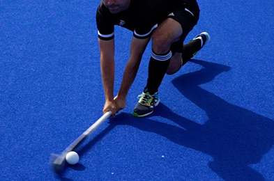 Field hockey player performing a fake flat pass on a blue pitch.