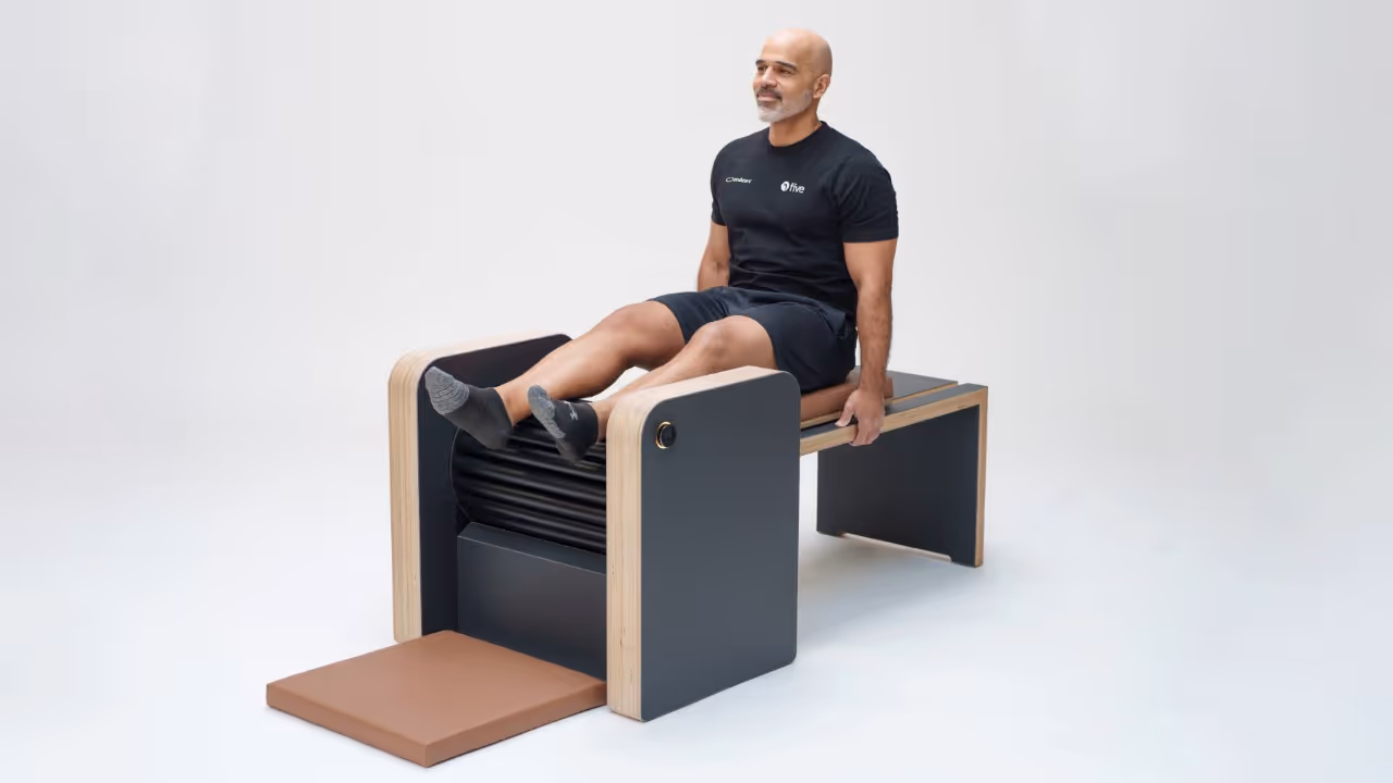 Mann in schwarzer Sportkleidung trainiert auf einem modernen Pilates-Gerät mit Holz und schwarzen Elementen.