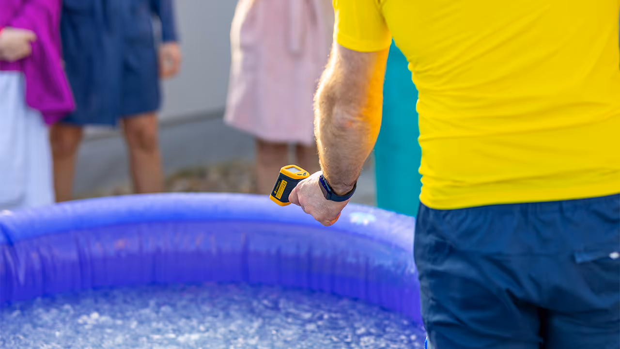 Mann in gelbem T-Shirt hält ein Infrarot-Thermometer vor ein Becken mit Eiswasser.