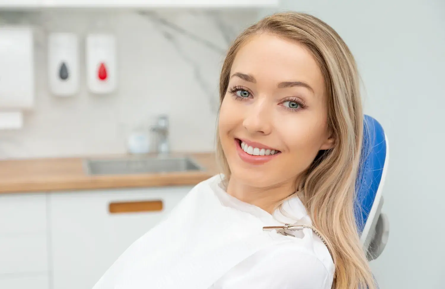 Woman smiling while sitting in a dentist's chair, wearing a dental bib.