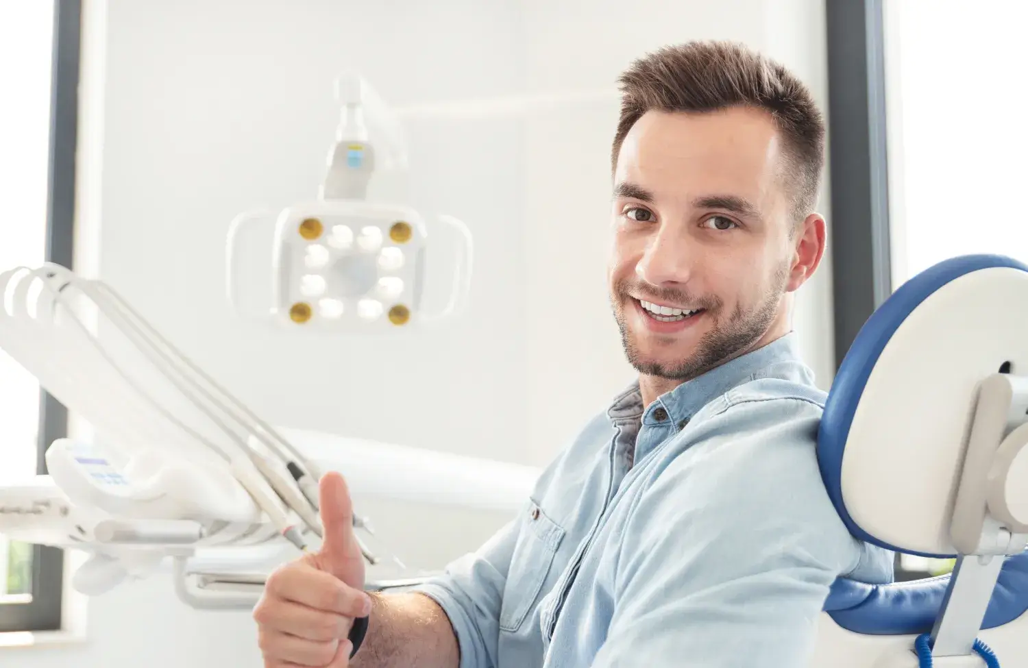 A person sitting in a dentist chair gives a thumbs-up and smiles at the camera.