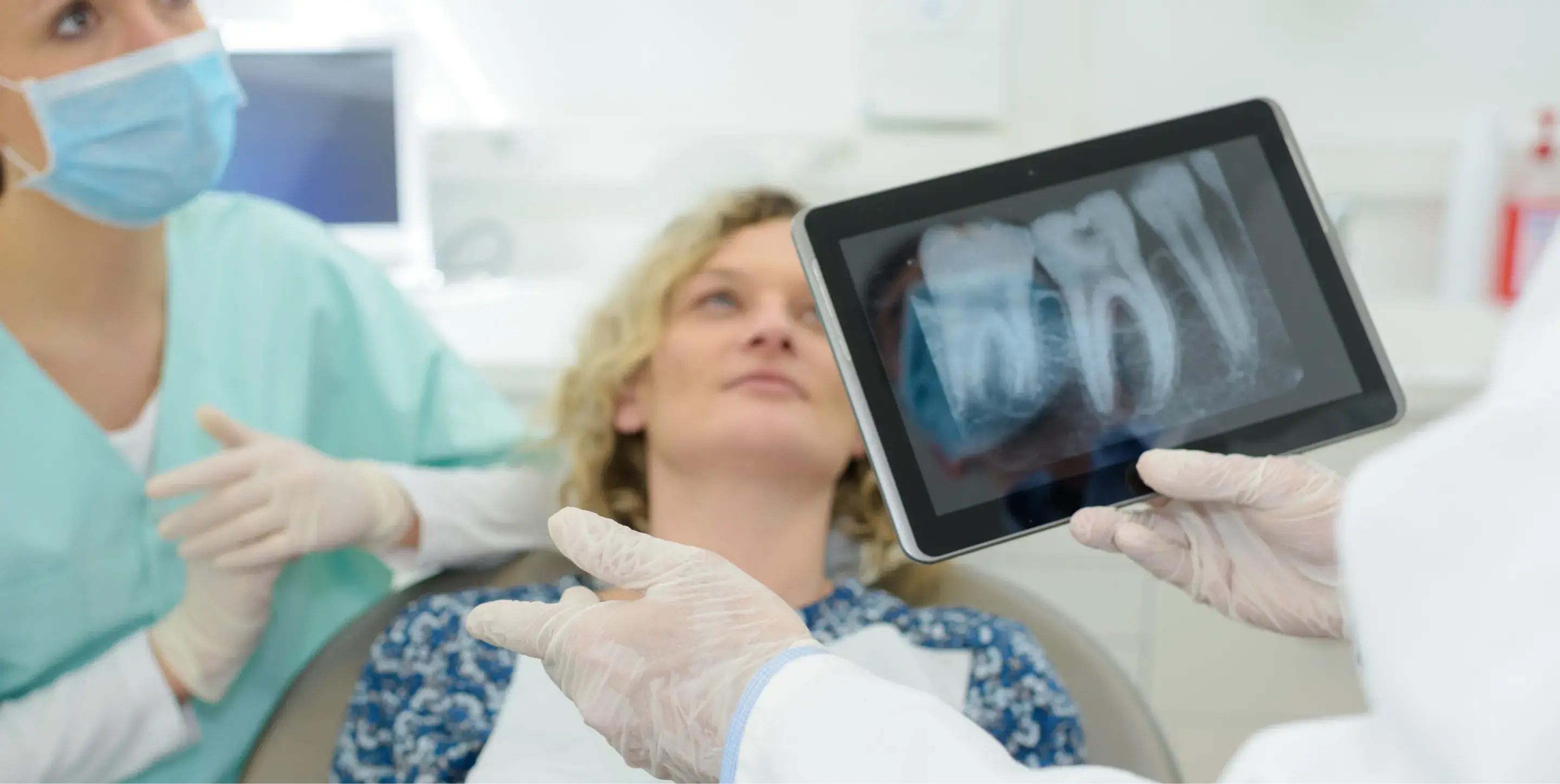 A dentist shows a dental X-ray on a tablet to a patient lying in the chair.