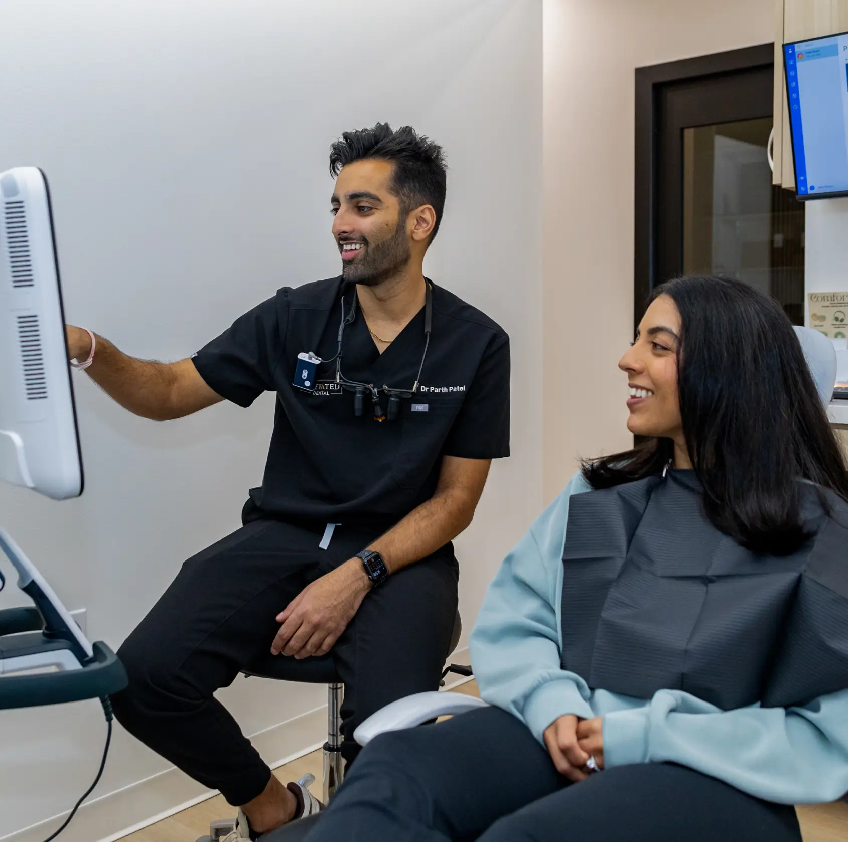 A person holds a mirror and smiles while a dental professional shows them clear aligners.