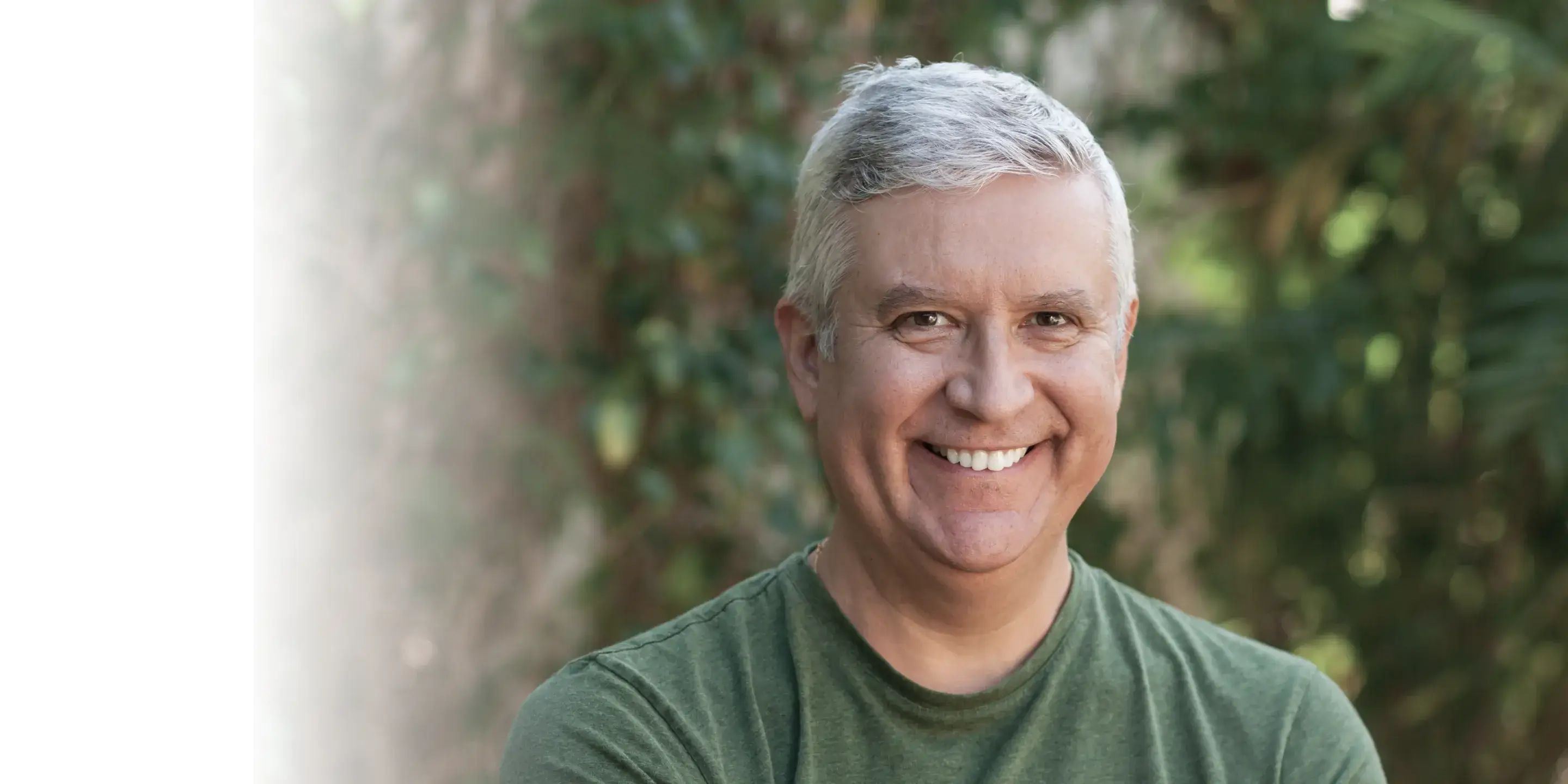 Smiling man with short gray hair in a green shirt, standing outdoors.
