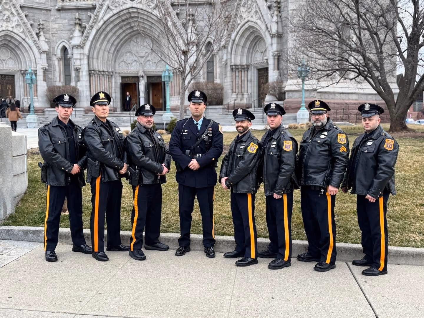 A group of eight police officers in uniform, standing in front of a grand architectural façade, posed for a photo.