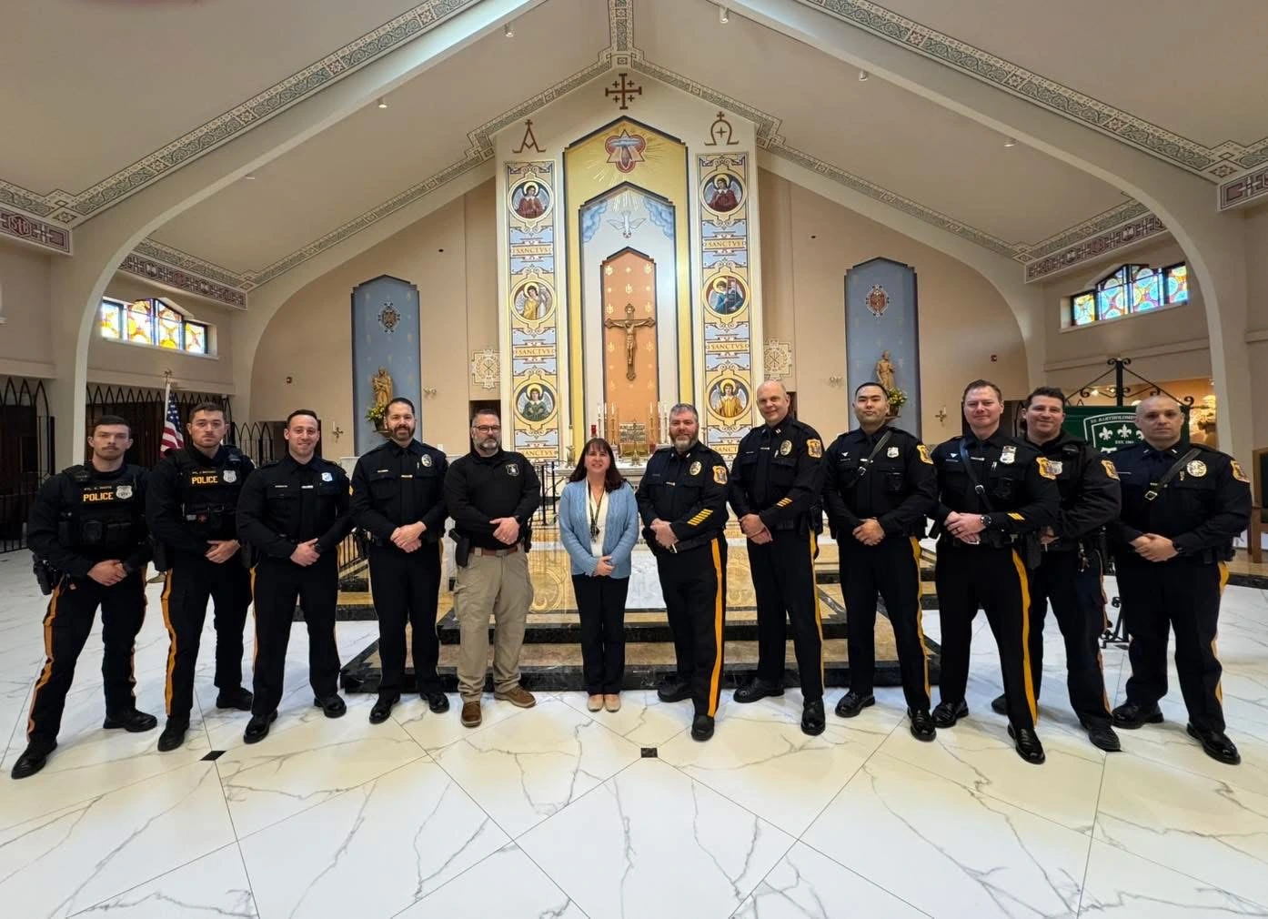 A group of police officers in uniforms stands in a church, with a decorative altar and stained glass in the background.