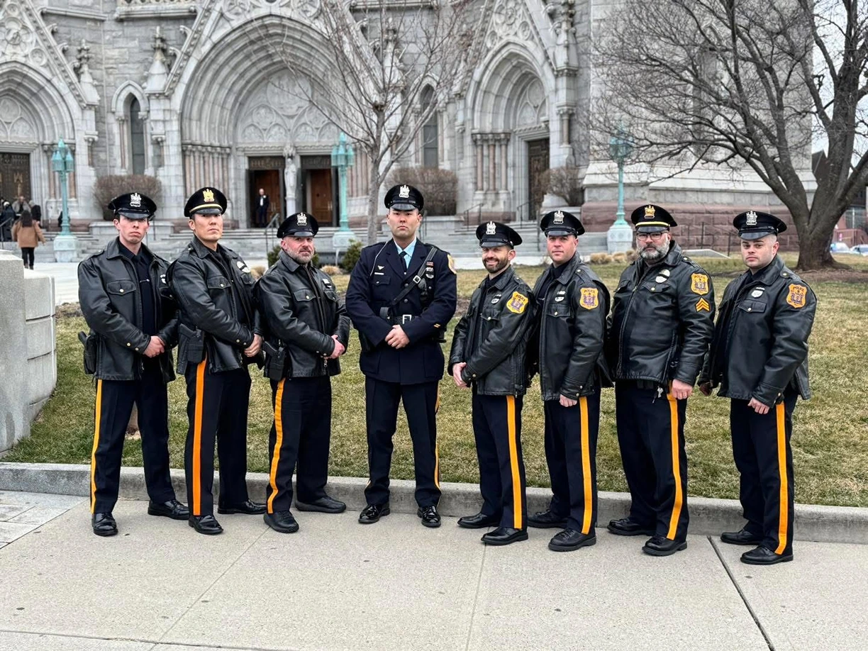 A group of uniformed police officers stand in a line outside a grand, stone building, showcasing various badges and uniforms.