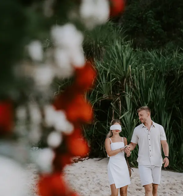 Couple français (femme avec les yeux bandés par un foulard blanc) qui marche main dans la main avant une demande en mariage sur la plage privée d'Uluwatu à Bali.