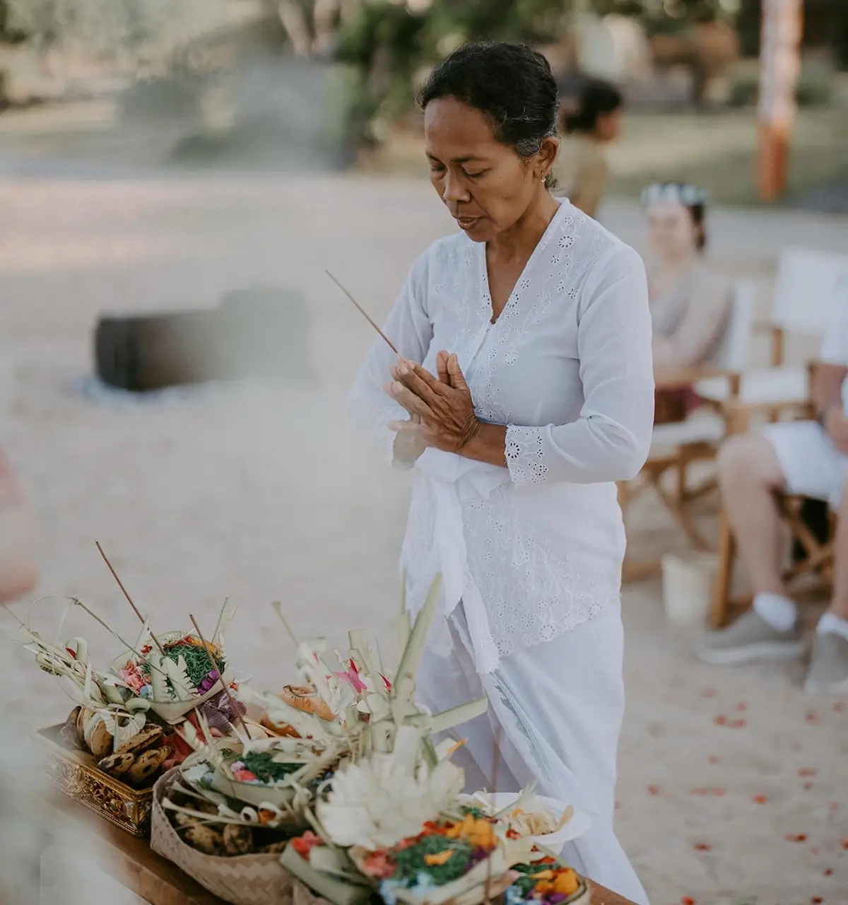 Cérémonie balinaise sur la plage à Bali, prêtresse locale réalisant un rituel traditionnel avec offrandes, ambiance sacrée et authentique.