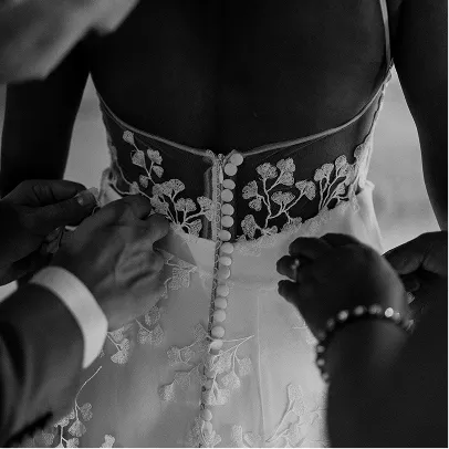 Détails en noir et blanc d'une robe de mariée avec des boutons blancs et des broderies florales, des mains ajustant la robe.