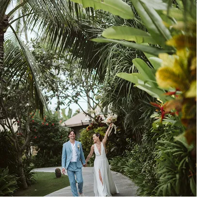 Couple de mariés belges marchant main dans la main sur un chemin entouré de végétation tropicale à Bali.