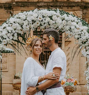 Couple français lors d'une cérémonie balinaise, entouré d'une arche de fleurs blanches.