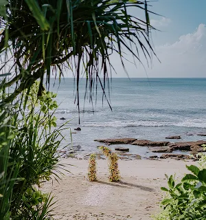 Arche de cérémonie florale sur une plage à Bali, avec vue sur l'océan, entourée de végétation tropicale.