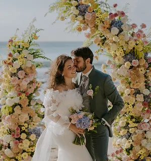 Couple de mariés heureux sous un arc de fleurs balinaises colorées sur une plage à Bali.