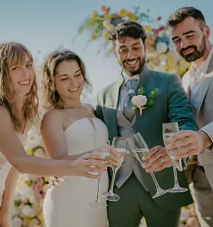 Un couple français et leurs deux amis heureux, portant des tenues élégantes, levant leurs verres pour un toast lors d'un mariage sous le soleil de Bali.