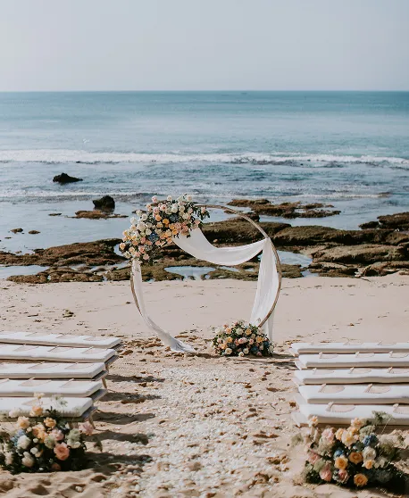 Arche blanche décorée de fleurs sur la plage avec vue mer pour mariage romantique à Bali.