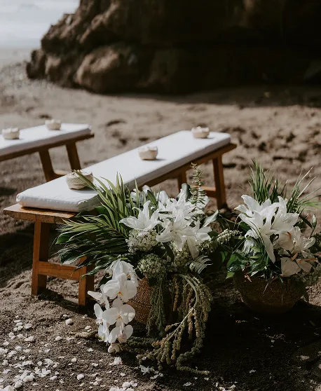 Bancs en bois décorés de lys blancs et orchidées pour cérémonie de mariage sur plage à Bali par une Wedding Planner Française.