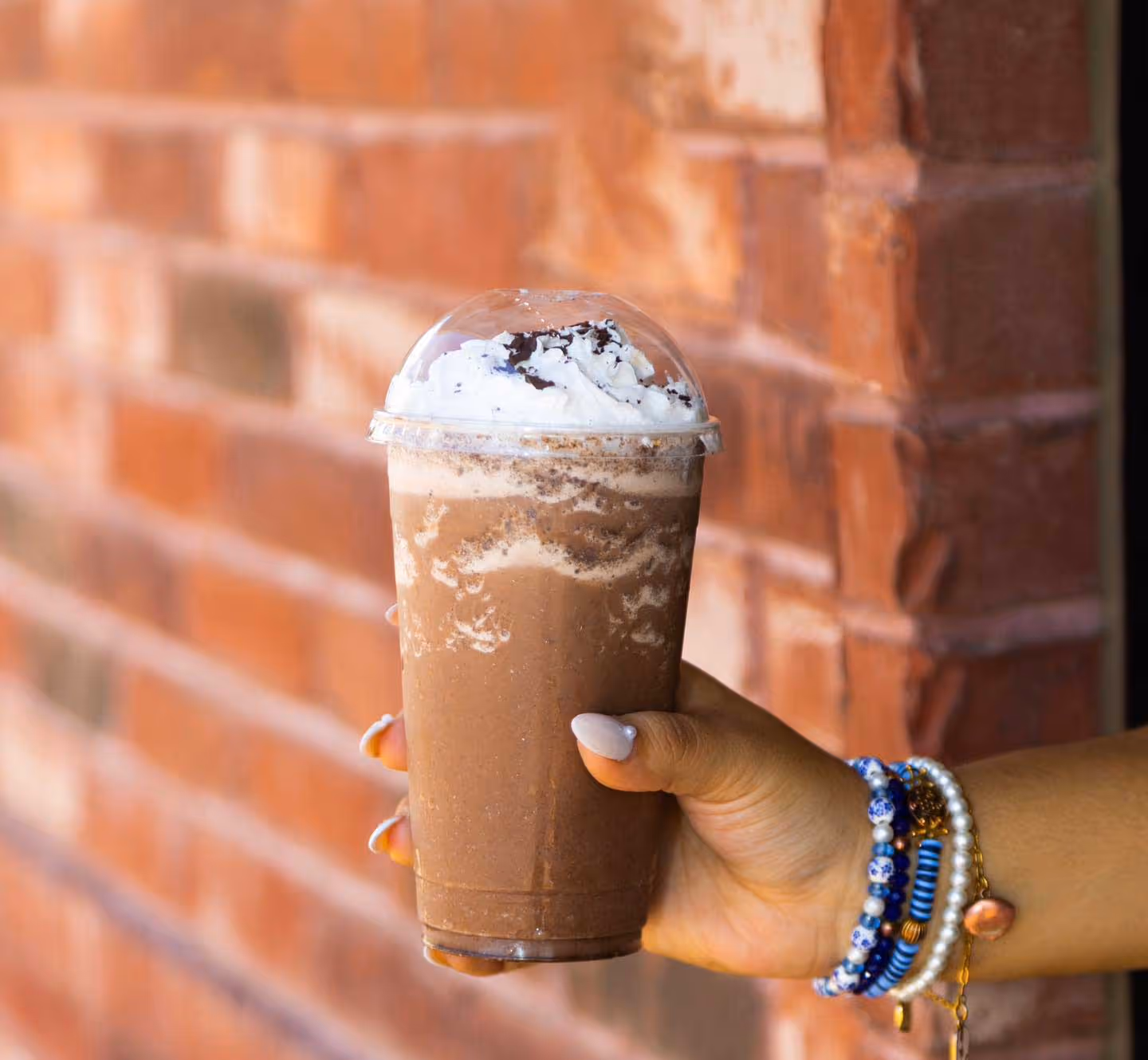 A person holding a chocolate milkshake in a cup.